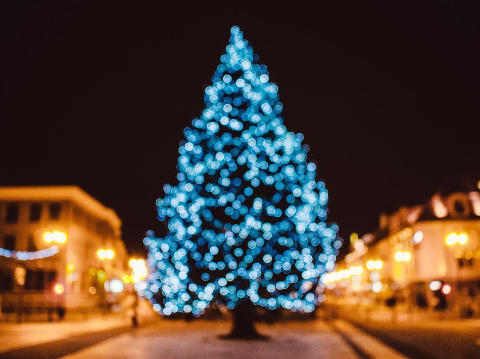 Free Image of Blurry Christmas tree covered in blue lights in a town. 