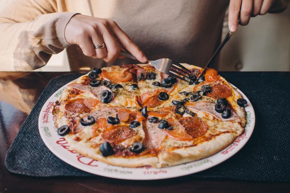 Free Image of Person cutting a pizza topped with olives and pepperoni 