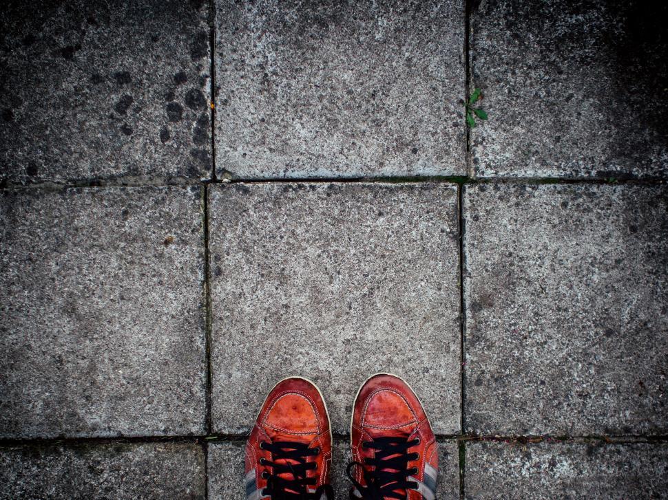 Free Image of Worn red sneakers standing on paved sidewalk tiles. 