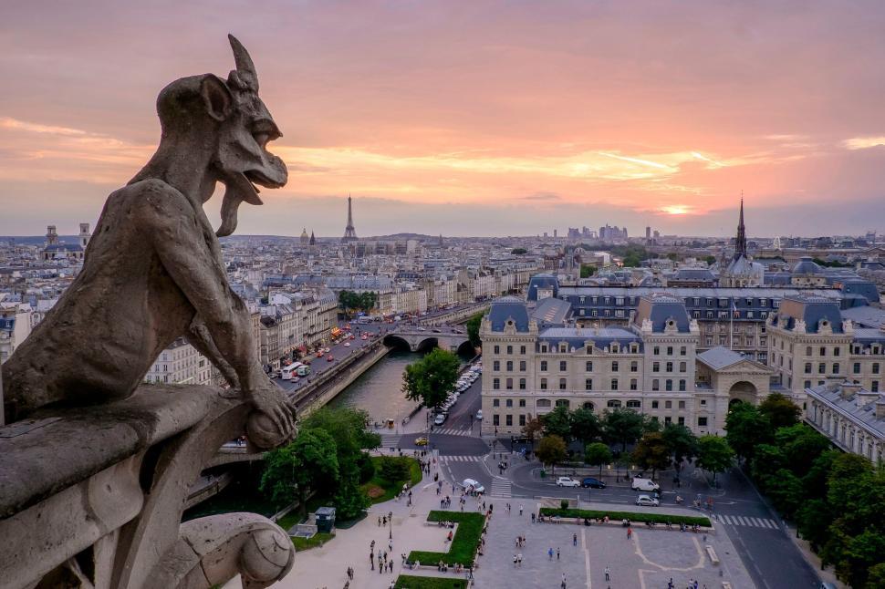 Free Image of Gargoyle watching over cityscape at sunset from a rooftop 