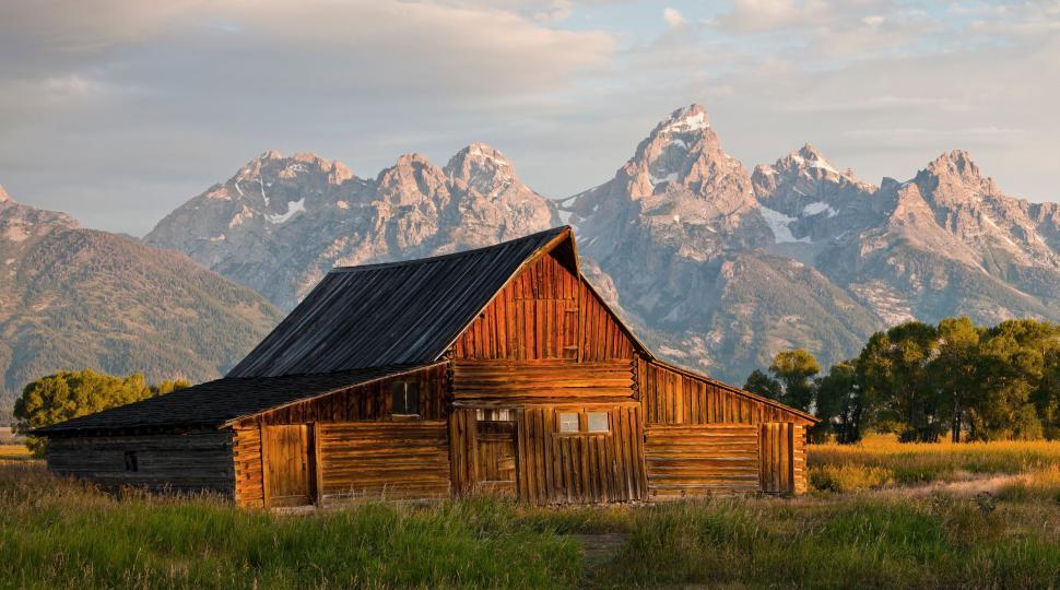 Free Image of Rustic barn with mountains under a dramatic sky. 
