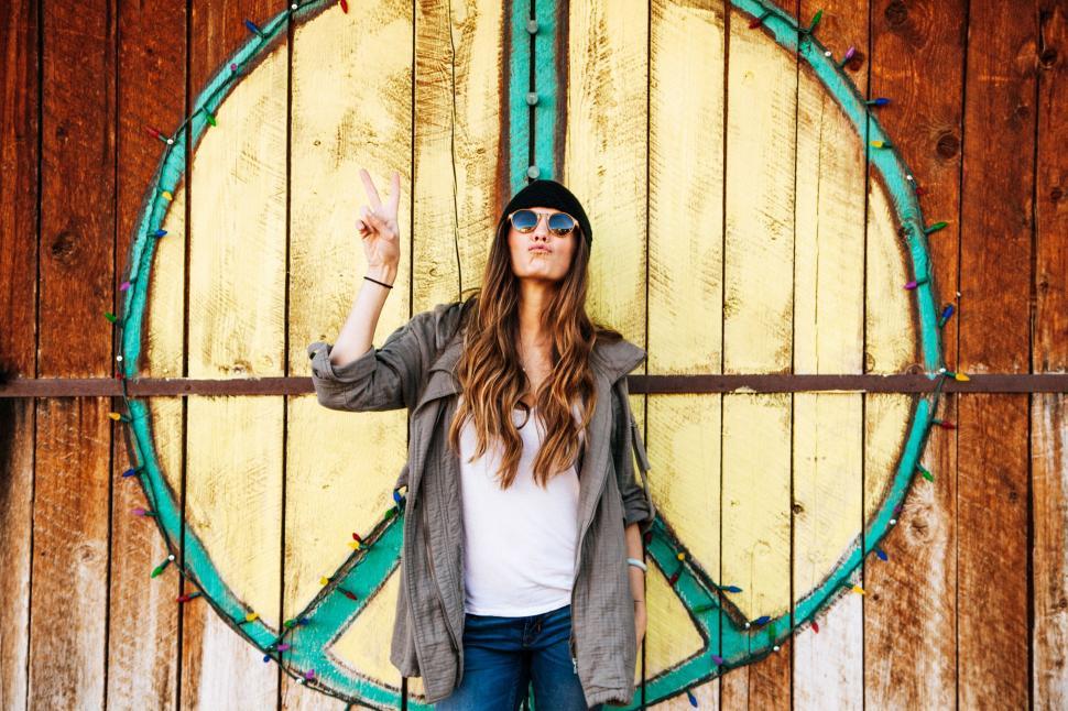 Free Image of Woman posing with peace sign in front of colorful mural 