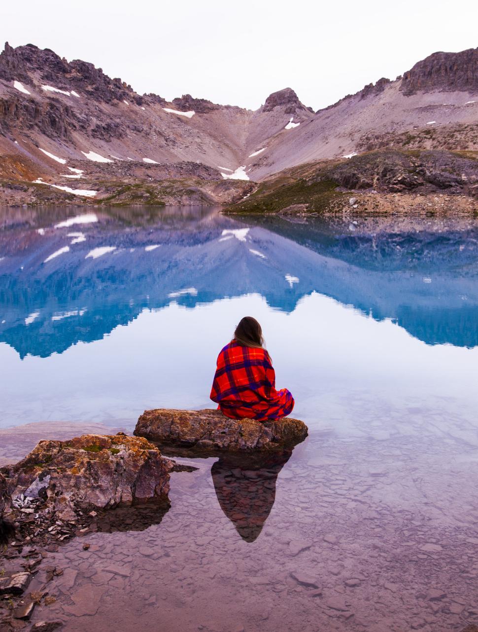 Free Image of Person in colorful blanket gazes at serene lake in mountains. 