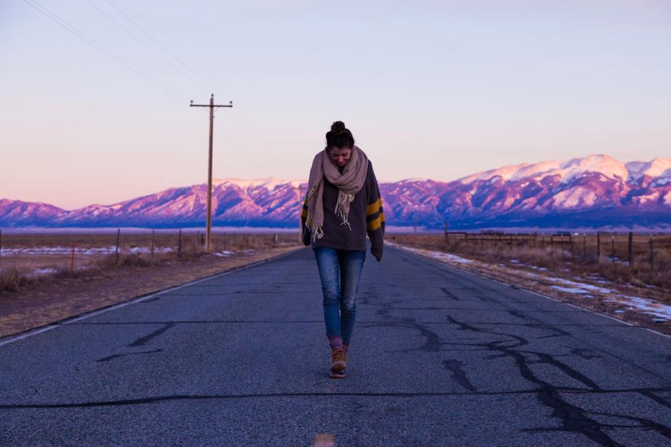 Free Image of Woman walking down an empty road towards mountains 