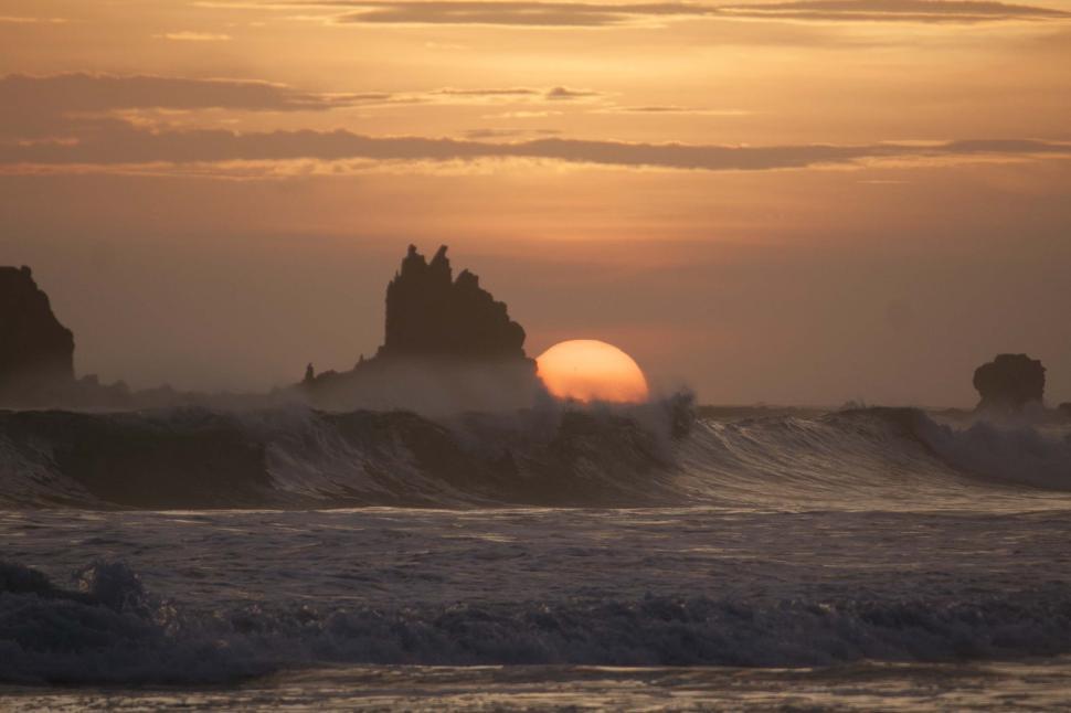 Free Image of Sunset over ocean waves with rocky formations visible 