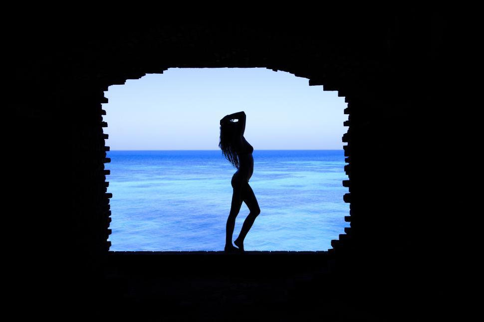 Free Image of Silhouette of woman by window with bright blue ocean 