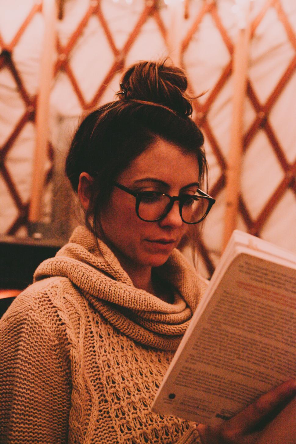 Free Image of Woman reading a book in cozy sweater by soft lighting 