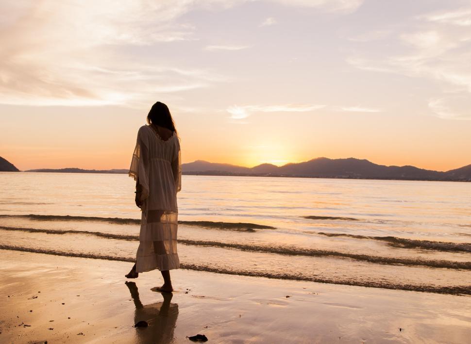 Free Image of Woman strolls on a serene beach during a beautiful sunset. 