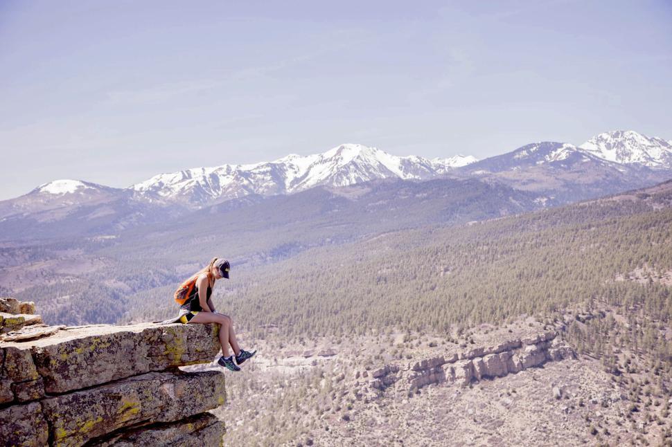 Free Image of Person sits on cliff edge with expansive mountain view. 
