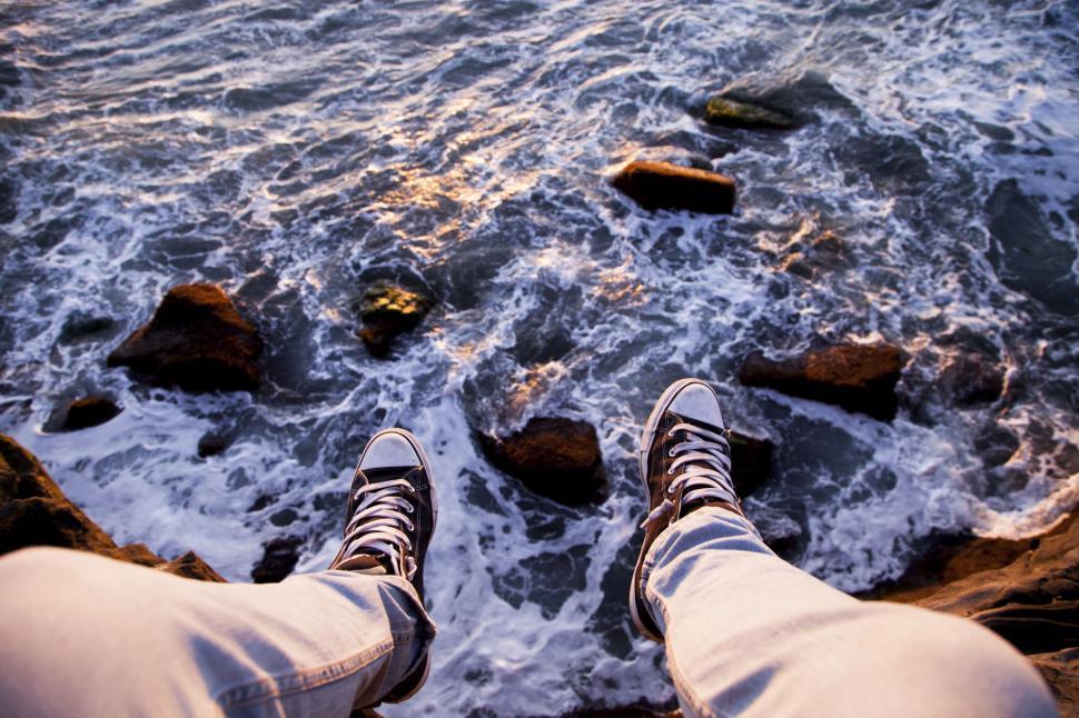 Free Image of Person sitting at edge of cliff above ocean waves. 