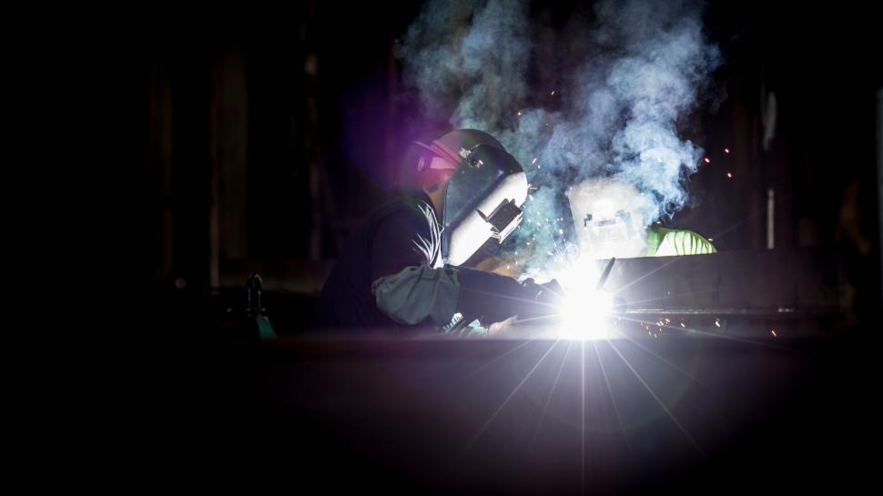 Free Image of Welder at work emitting bright sparks in dark workshop. 