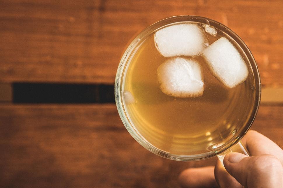Free Image of Glass of icy beverage held against a wooden table. 
