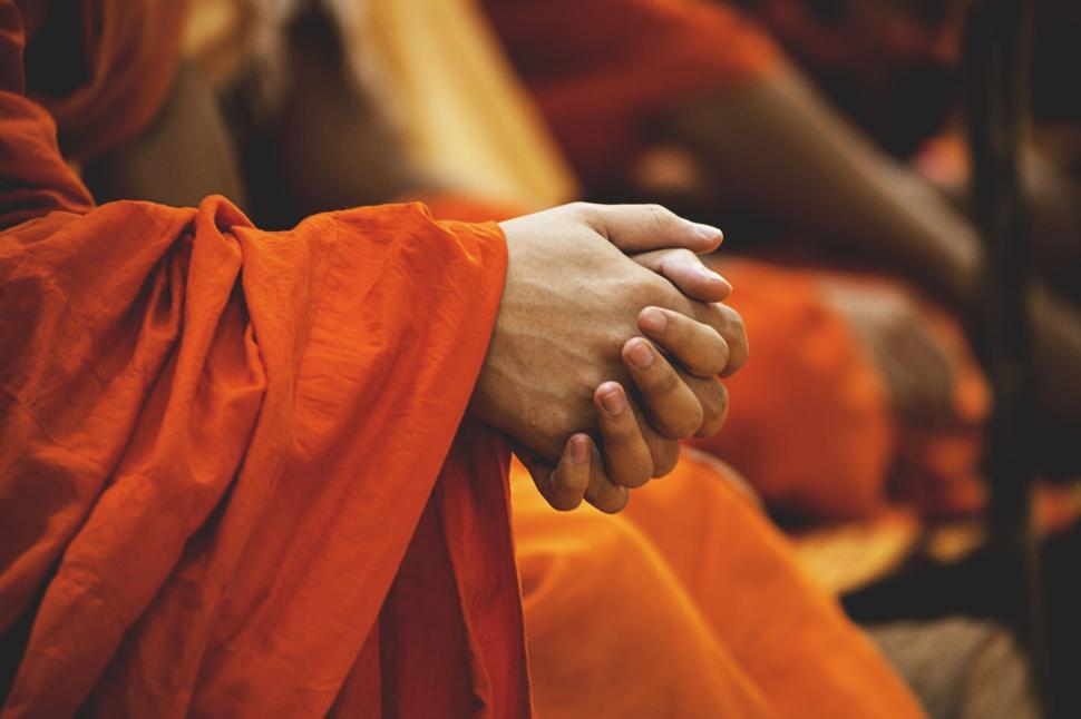 Free Image of Hands clasped in prayer within vibrant orange robes. 