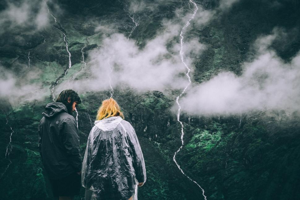 Free Image of Two hikers in raincoats overlooking a mist-covered valley. 