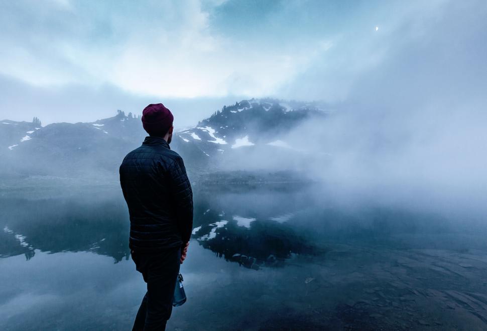 Free Image of Person standing near foggy lake with mountains behind 