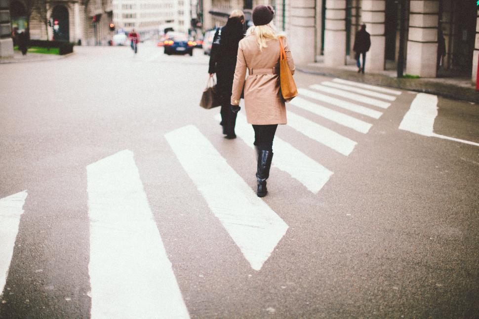 Free Image of Person crossing city street wearing trench coat and hat 