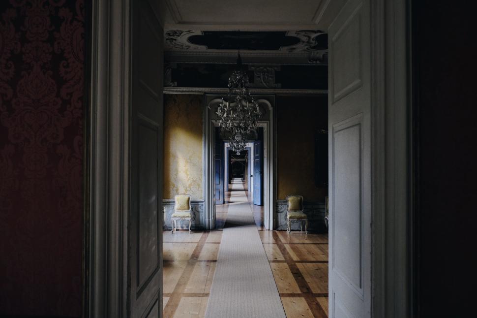 Free Image of Long hallway with chandeliers and distant open doors. 