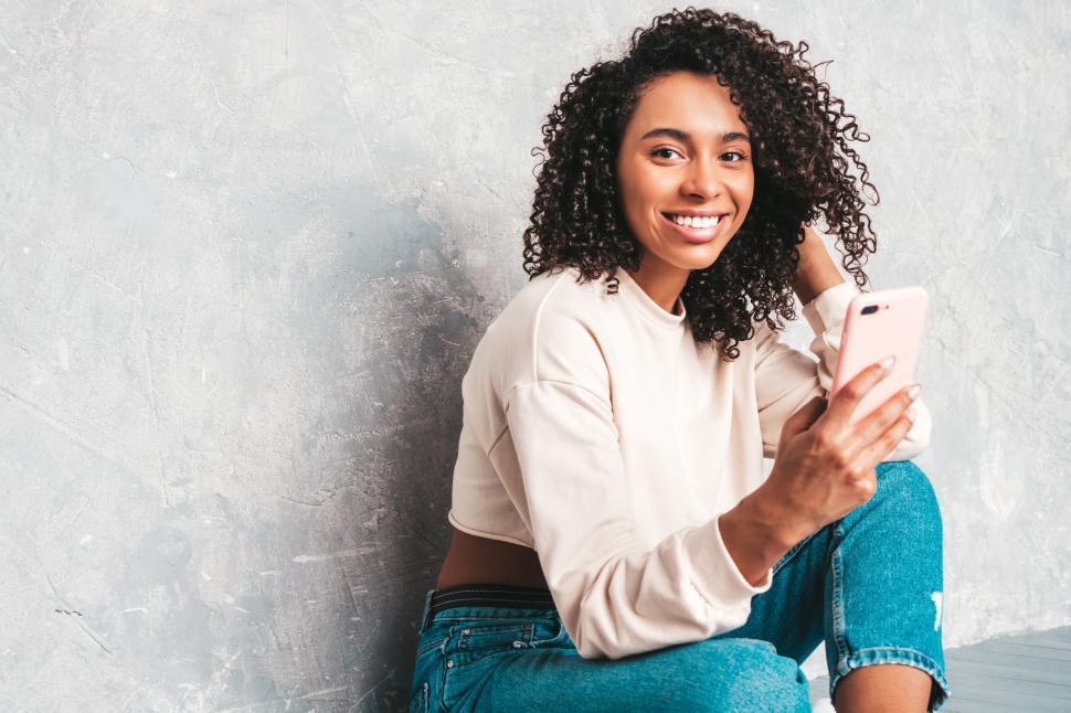 Free Image of Smiling woman holding pink phone, casual indoor pose 