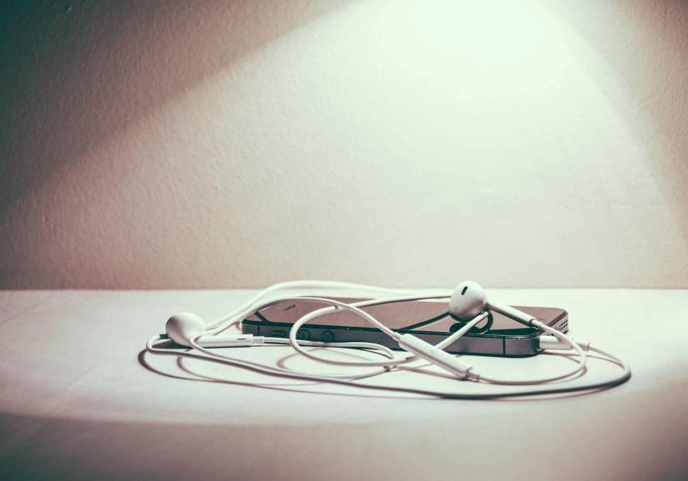Free Image of Earbuds and smartphone on white surface under soft light 