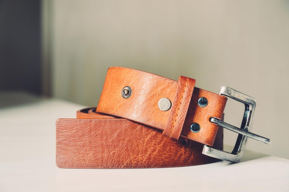 Free Image of Brown leather belt with buckle coiled on white surface 