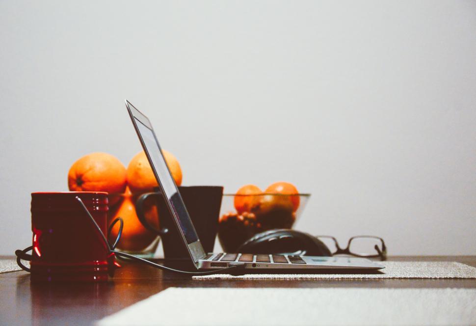 Free Image of Laptop, mug, and fruits on a wooden desk with accessories 