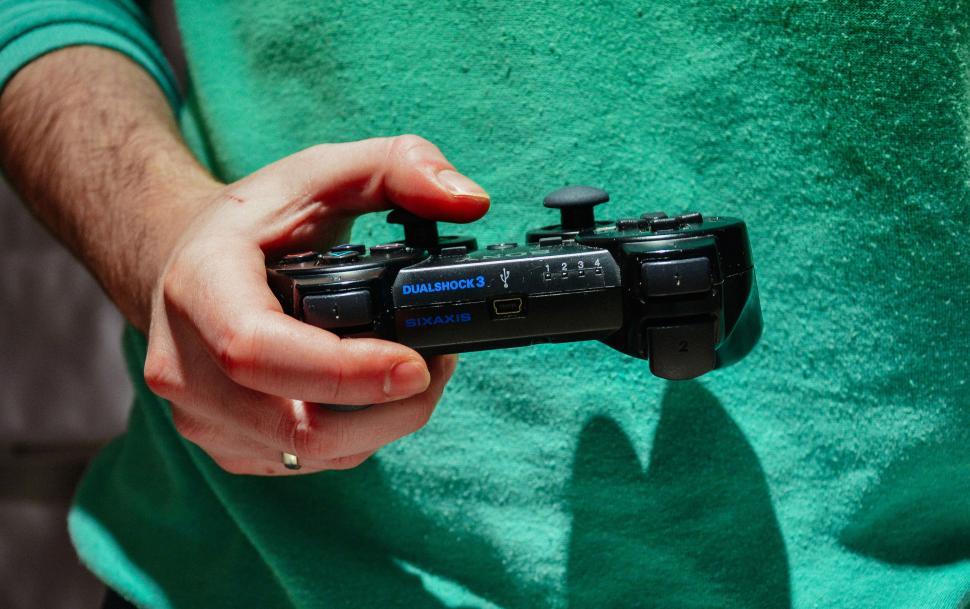 Free Image of Hand holding a black gaming controller in casual setting 