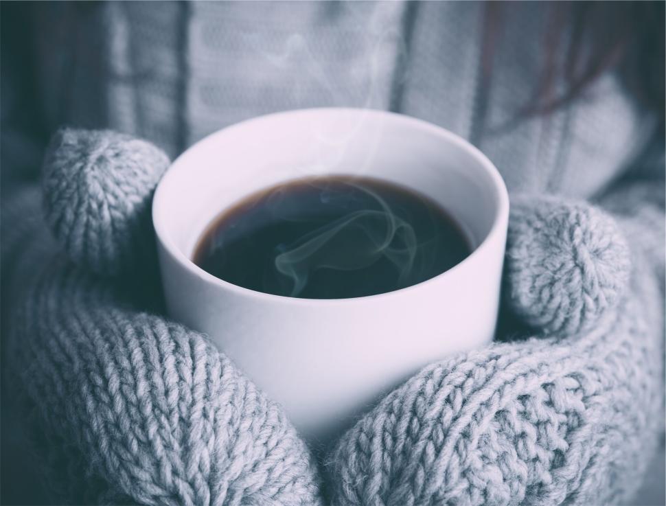 Free Image of Hands in knit gloves holding a steaming cup of coffee 