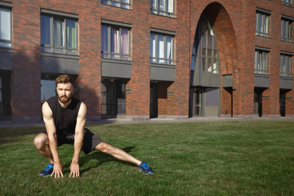 Free Image of Sports, fitness, wellbeing, endurance and determination concept. Confident young Caucasian male jogger focused on training, doing side lunge on green grass, stretching legs before cardio exercise 