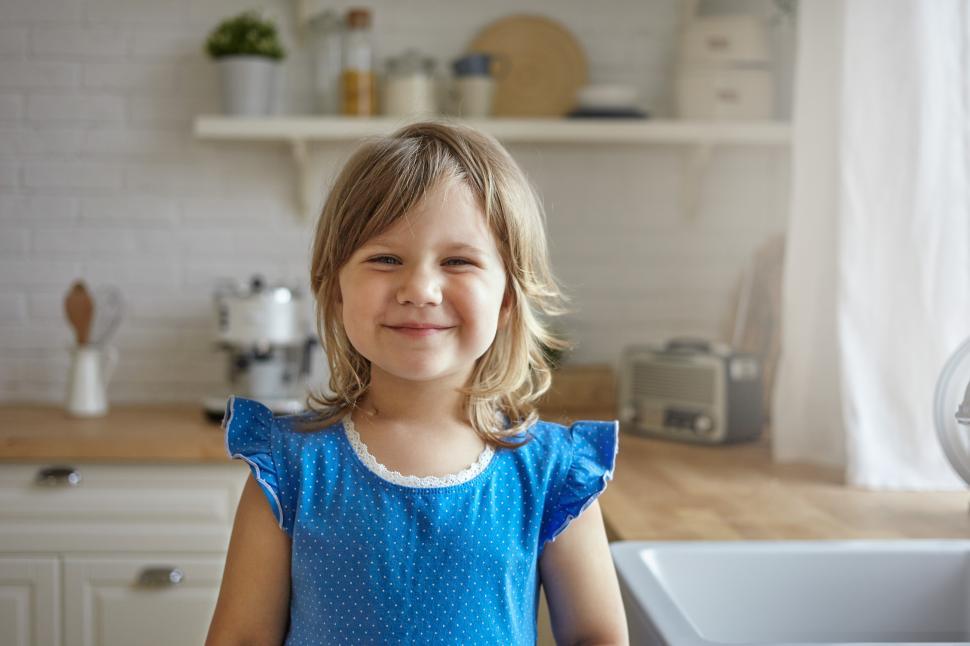 Free Image of Indoor shot of beautiful funny little girl with fair hair and soft skin smiling joyfully at camera, expressing positive emotions and joy, wearing cute blue dress. Childhood, happiness and innocence 