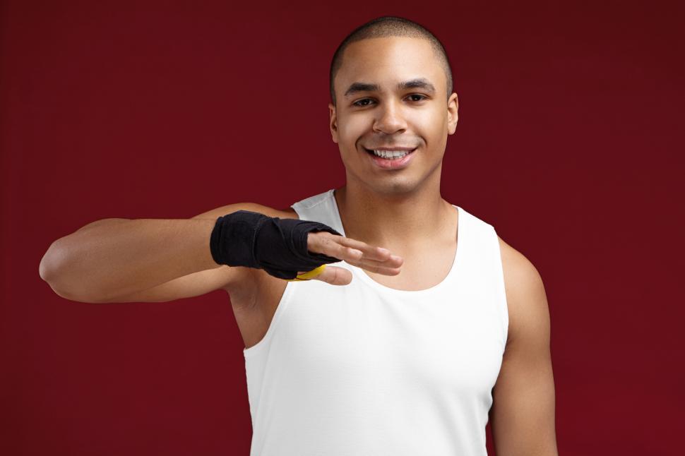 Free Image of Sports, strength, power and motivation concept. Portrait of handsome young African American male kick-boxer preparing his fists for fight, applying black boxing bandages, having concentrated look 