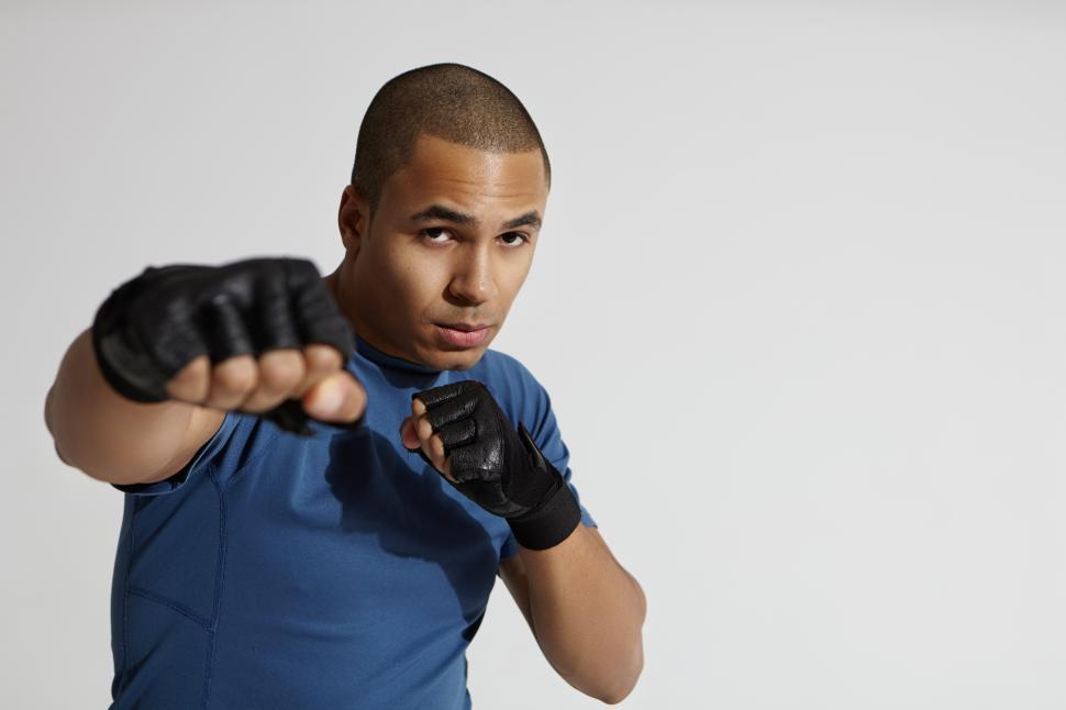 Free Image of Portrait of attractive young mixed race male with shaved head exercising in gym, standing at white wall, aiming pumped fist at camera, throwing punch. Boxing, kickboxing and martial arts concept 