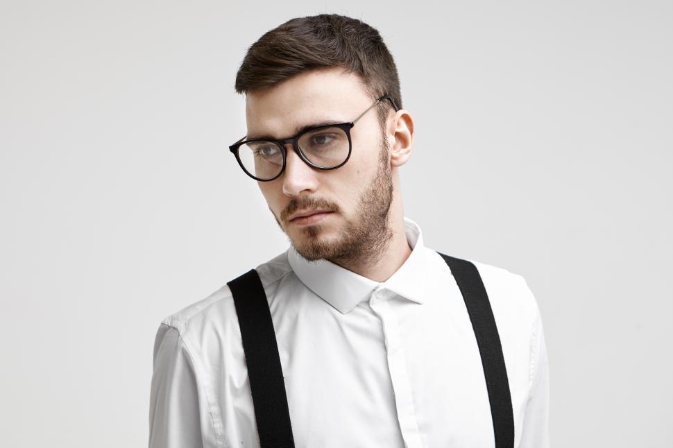 Free Image of Picture of thoughtful good looking young Caucasian businessman with trimmed beard and mustache standing at white office wall, having serious thoughtful look. Business, style and success concept 
