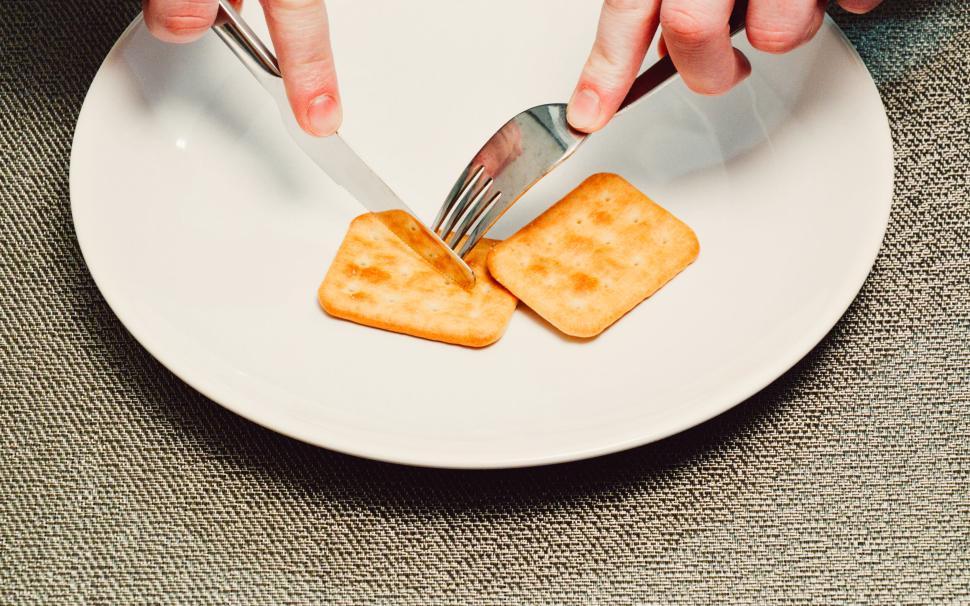 Free Image of Person about to cut a cracker on a plate using cutlery 