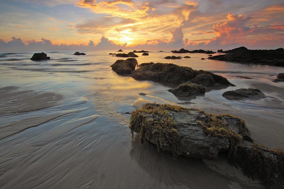 Free Image of Sunset over rocky seashore with dramatic clouds above 