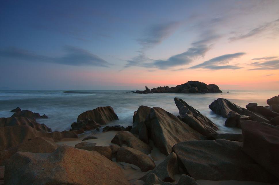 Free Image of Rocky shore with calm waves and sweeping clouds at dawn. 