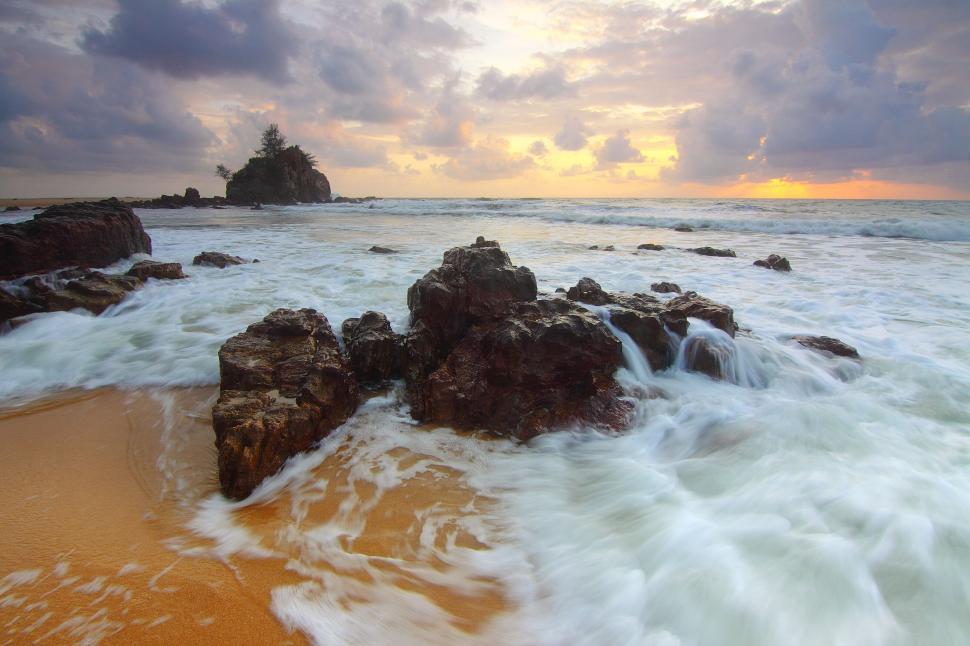 Free Image of Waves crashing on rocky beach under dramatic cloudy sky. 