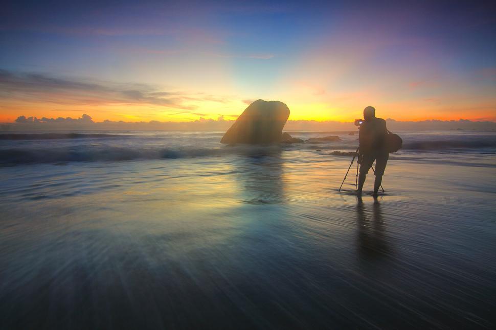 Free Image of Photographer capturing a sunset on a rocky beach. 