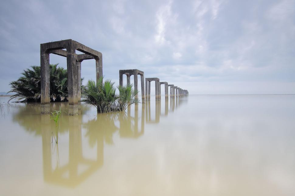 Free Image of Old pier ruins in water with reflections of cloudy sky. 