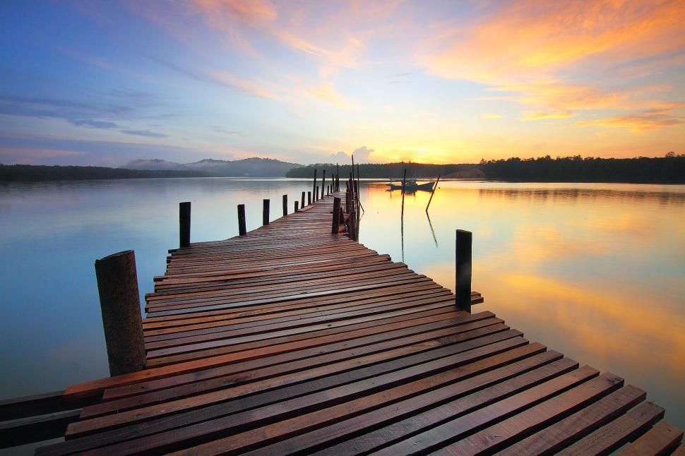 Free Image of Wooden pier extending into lake at sunset with boat. 