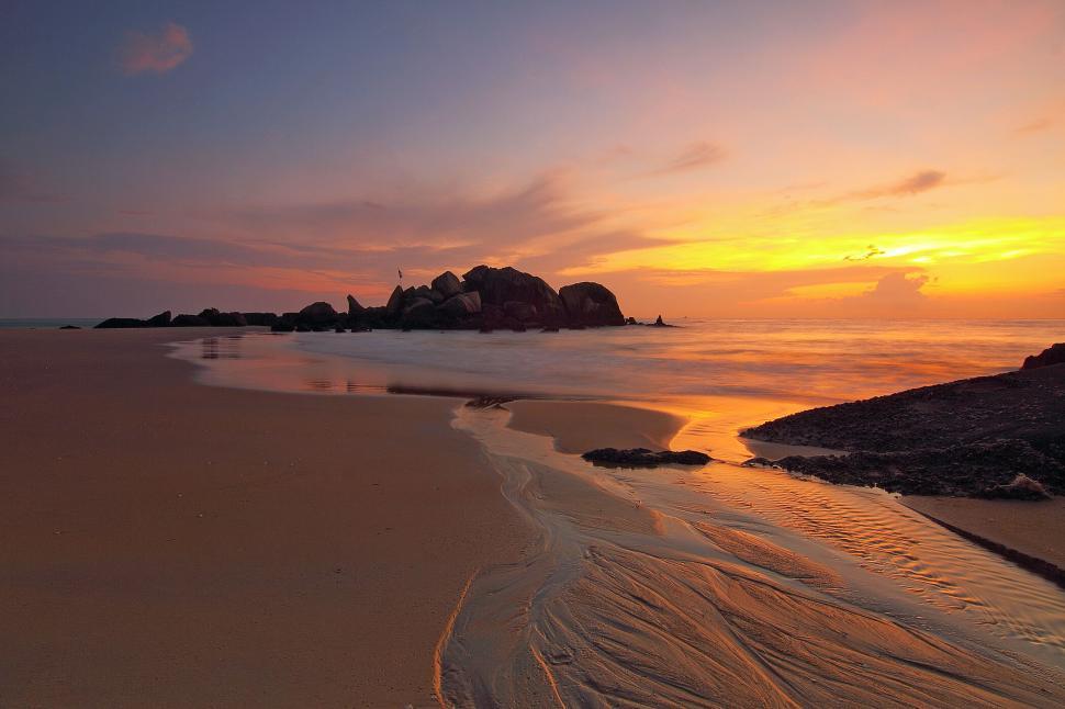 Free Image of Golden sunset on a serene beach with rocky formations 