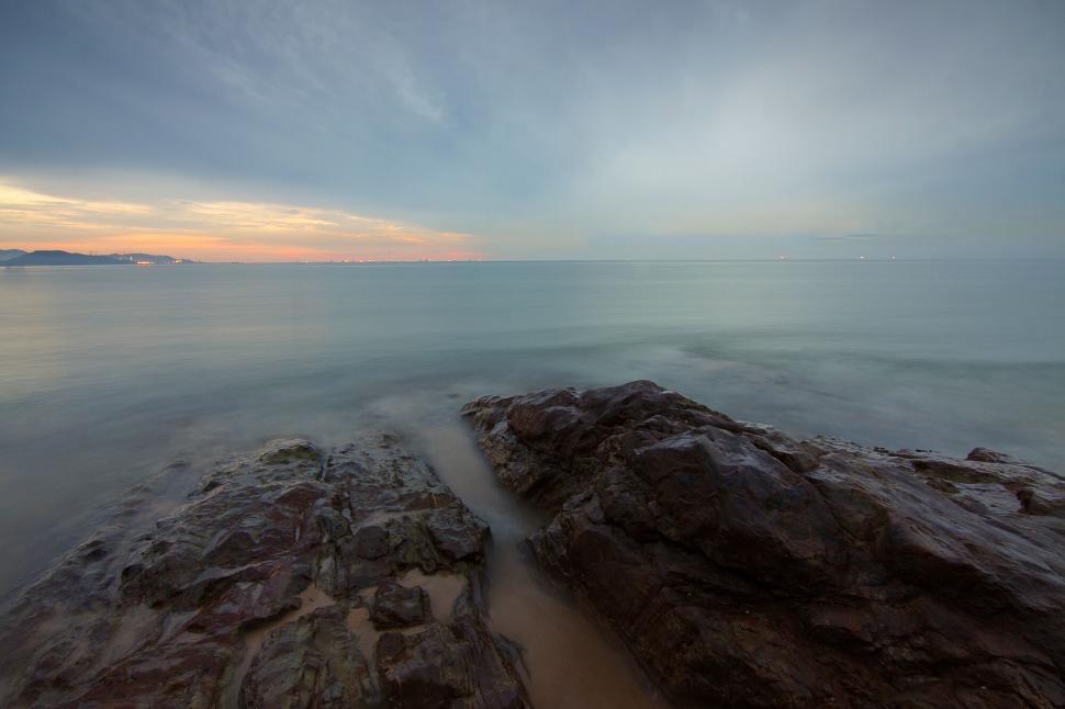 Free Image of Serene seaside sunrise view with rocky beach foreground 