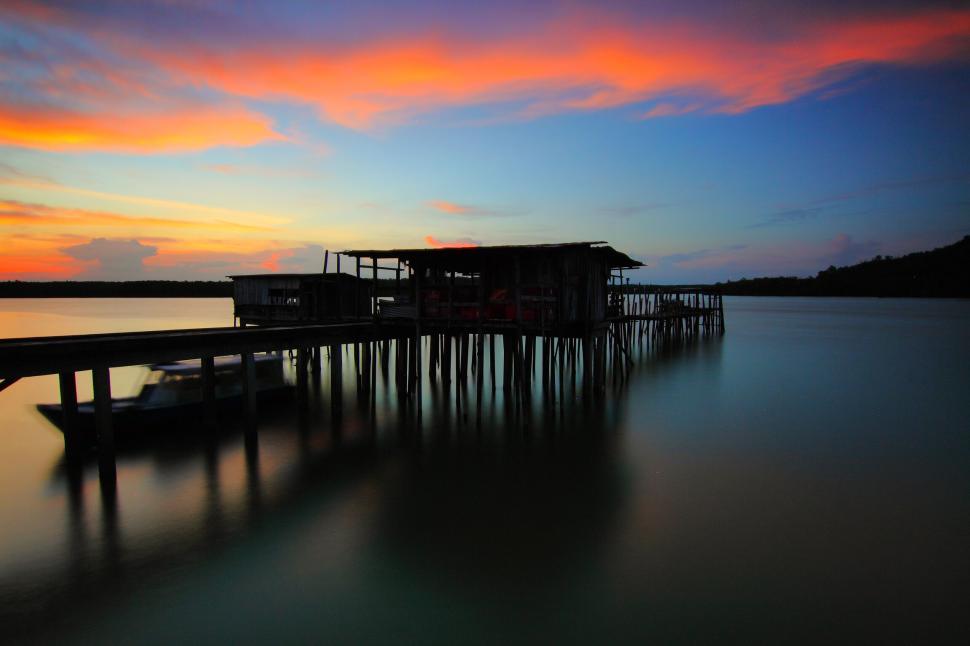 Free Image of Sunset over wooden pier casting reflections in water 