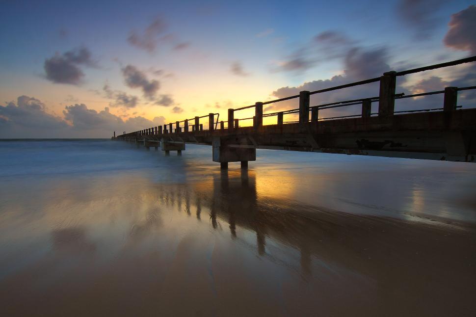 Free Image of Sunrise over coastal pier with reflections in ocean water 