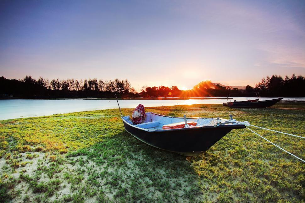Free Image of A lonely boat sitting on grassy lake shore at sunset 
