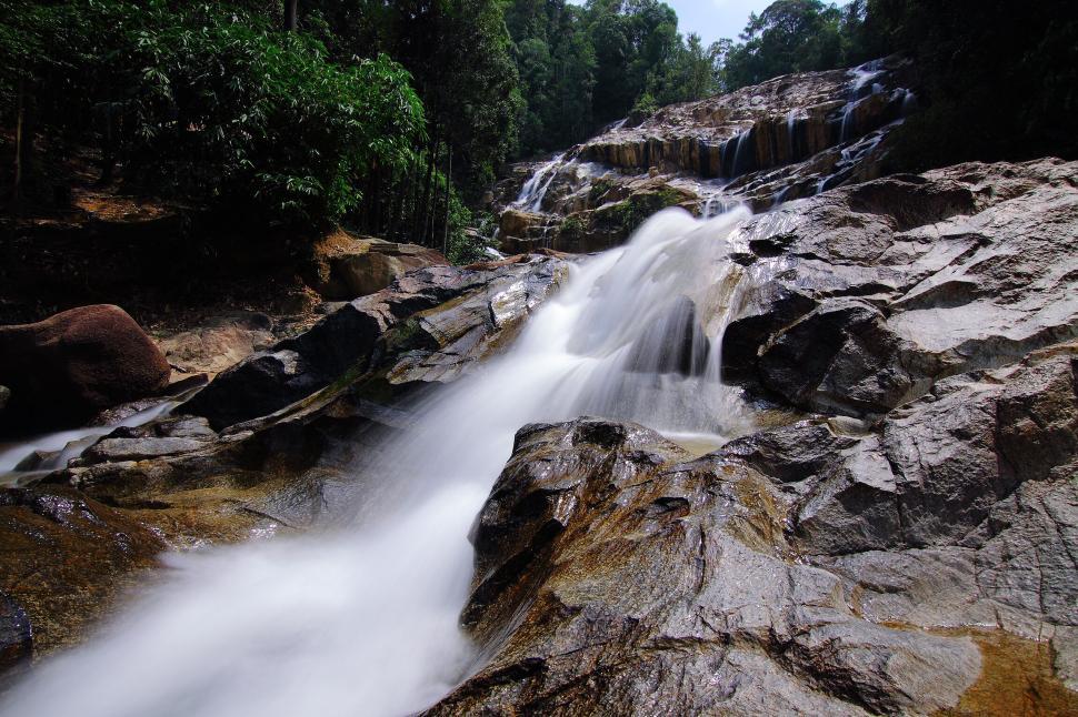 Free Image of A pristine rocky waterfall flows through dense forest 
