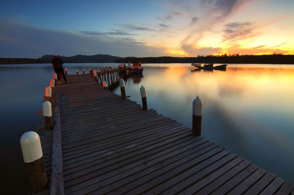 Free Image of Long wooden pier extends out onto calm reflective lake 
