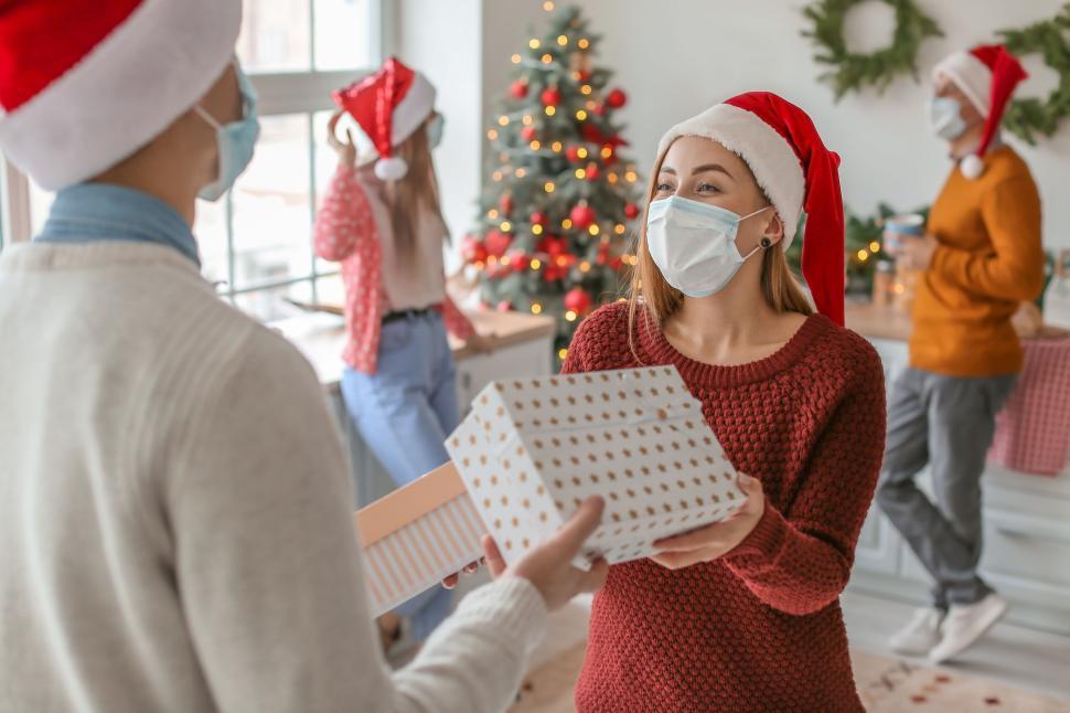 Free Image of Masked individuals exchanging Christmas presents indoors. 