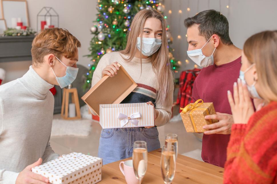 Free Image of Friends exchange gifts wearing masks near Christmas tree 
