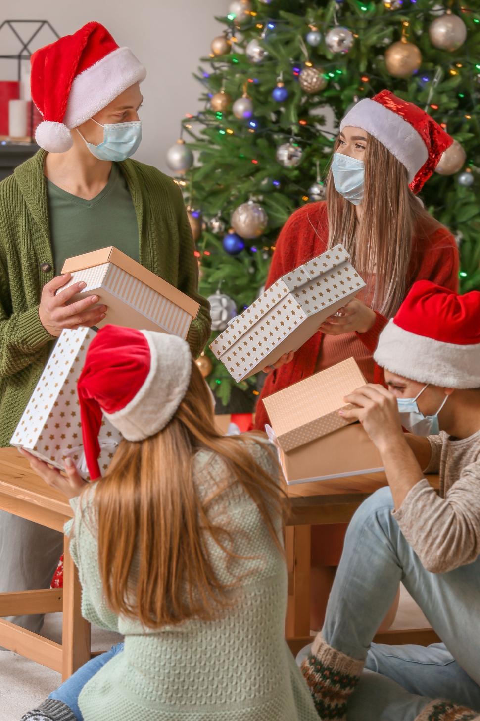 Free Image of Group of friends exchange gifts in front of Christmas tree. 