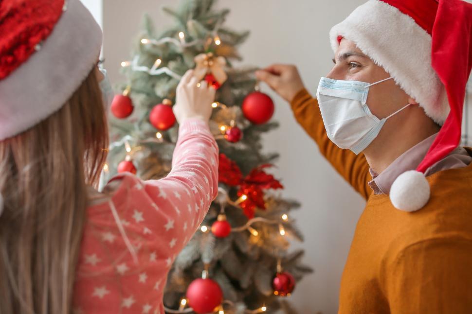 Free Image of Couple decorates Christmas tree with red ornaments happily. 